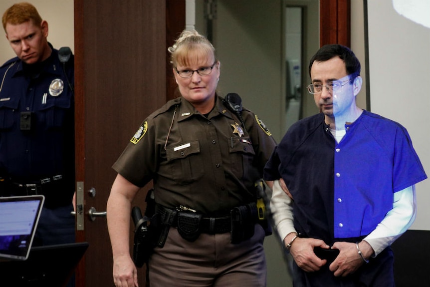 A security guard leads a shackled Larry Nasser into court