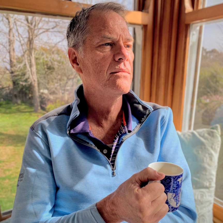 A man in a blue shirt holds a cup of coffee.