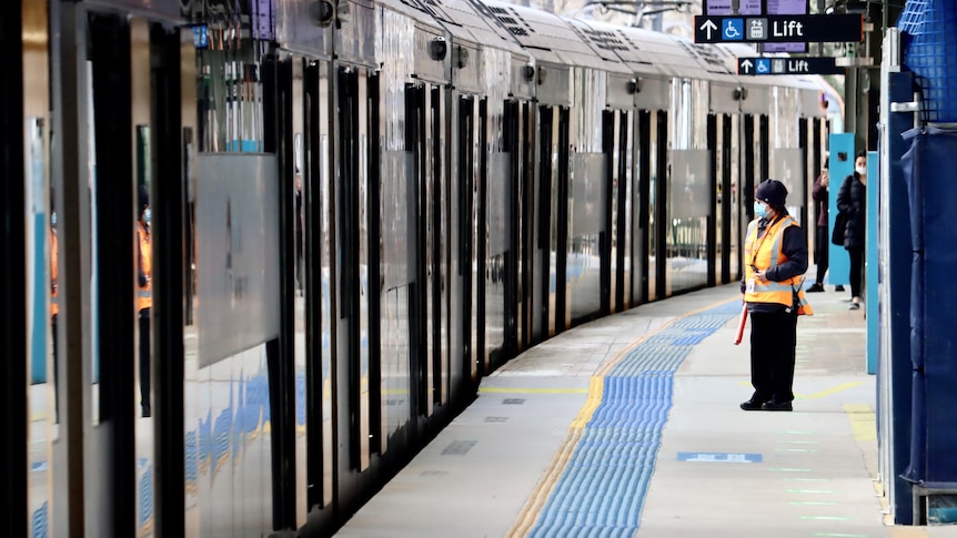 Uma pessoa de paletó alto e máscara em pé na plataforma do trem