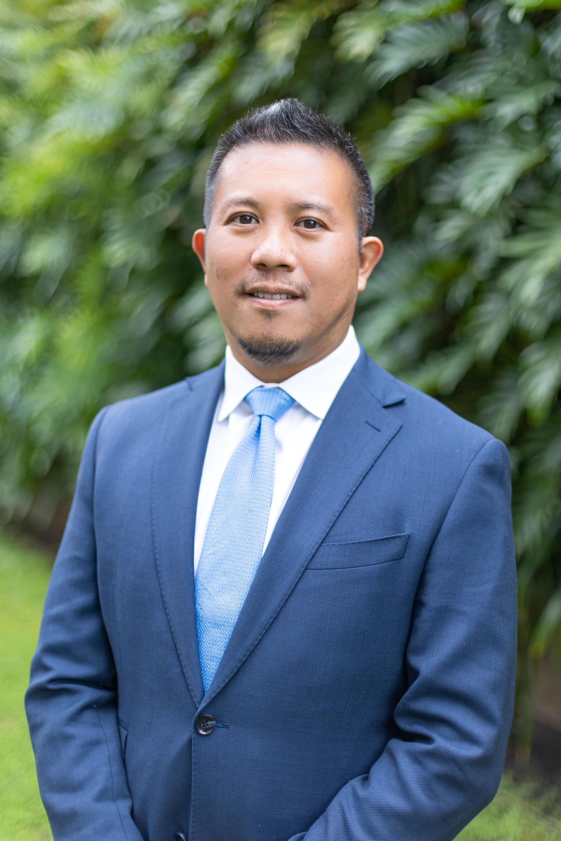 A man wearing navy suits and smiling to the camera.