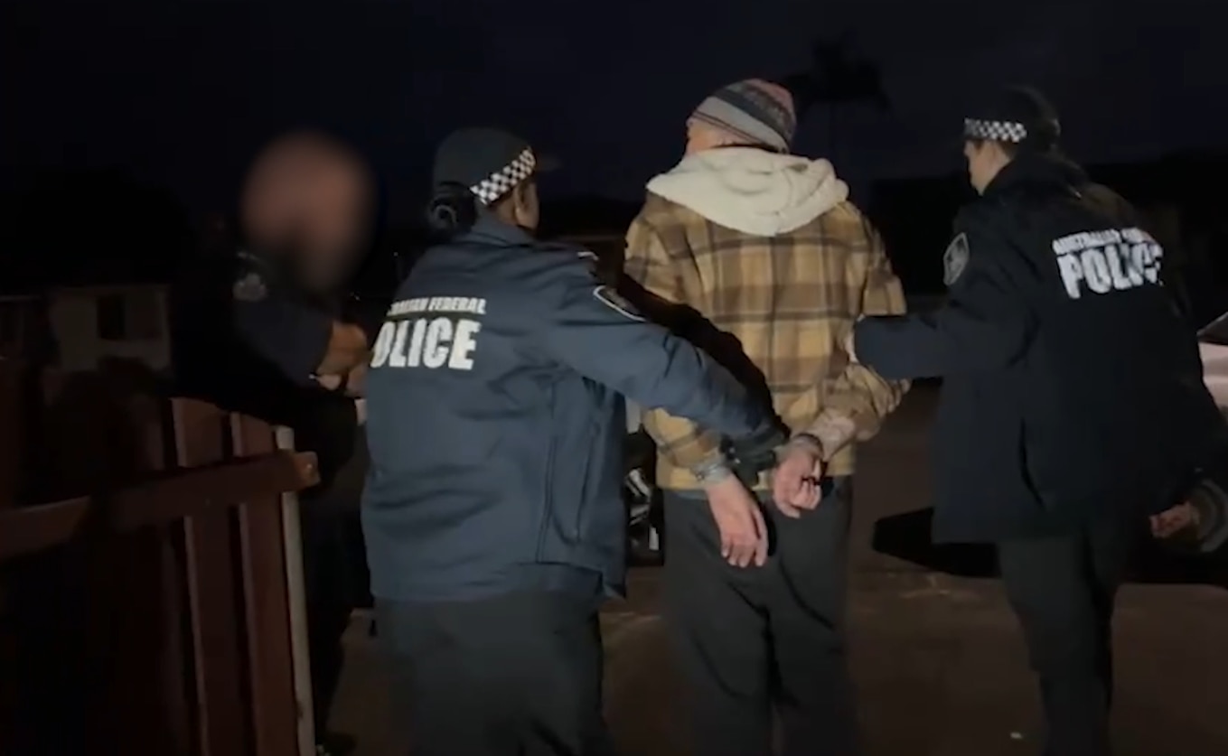Man wearing beanie being escorted by AFP officers