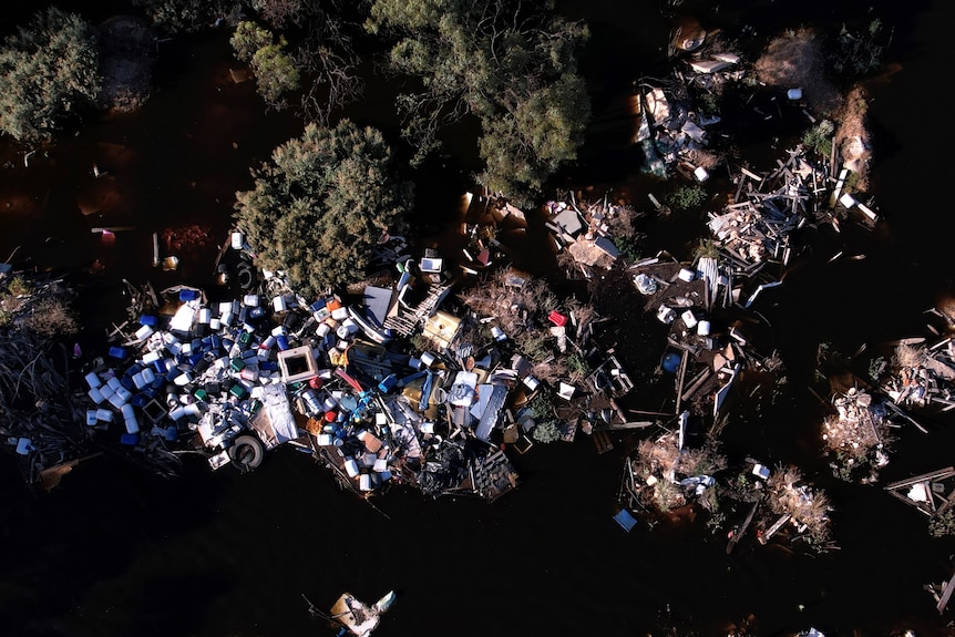 An aerial photo of lots of rubbish piled together in dark river waters surrounded by trees
