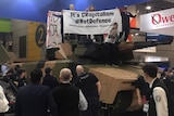 Protesters on top of a tank hold out a banner as police and security look on