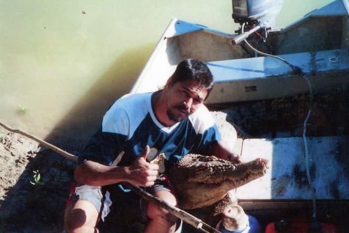 Indigenous man holds a crocodile head while sitting in a boat.