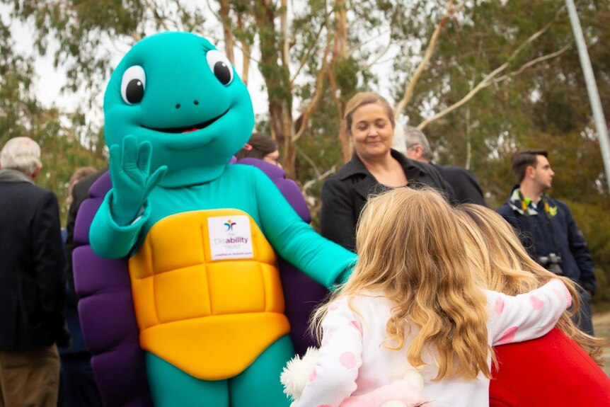 The turtle mascot for The Disability Trust is waving at a young girl