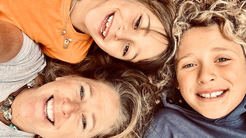 A selfie of Laura and her two children smiling and lying on the ground