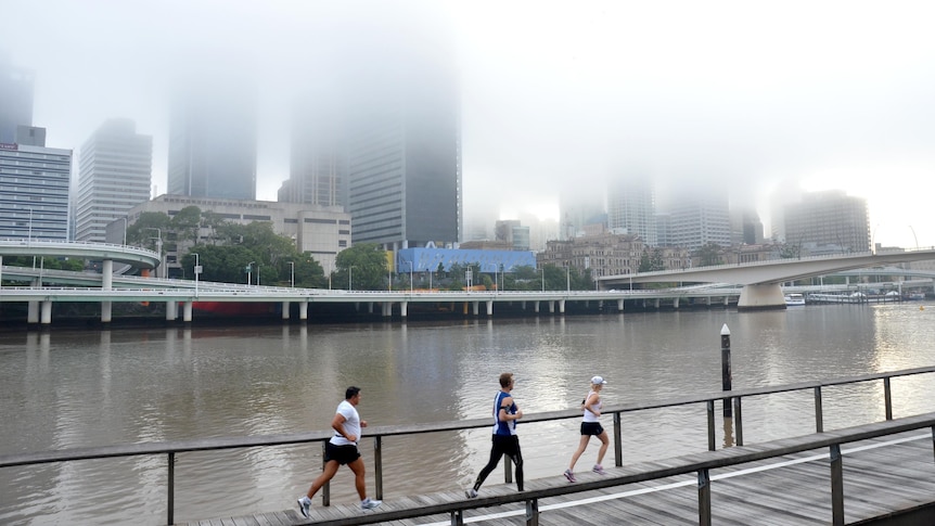 Early morning joggers run along the Brisbane River as a mist hangs over the CBD.