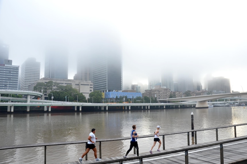 Early morning joggers run along the Brisbane River as a mist hangs over the CBD.