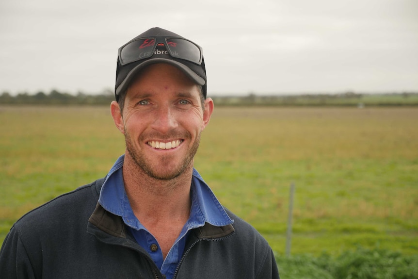 A smiling man in his thirties in a baseball cap stands smiling in a paddock
