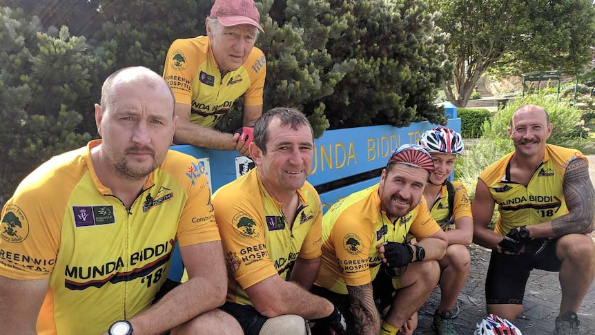 A group of cyclists wearing yellow jerseys crouching on the ground.