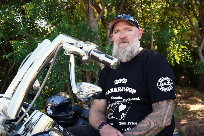 A man with a large build stands next to his motorbike.
