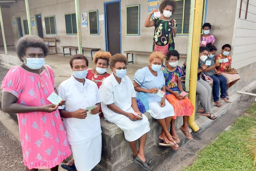 A group of women wearing masks hold pieces of paper.