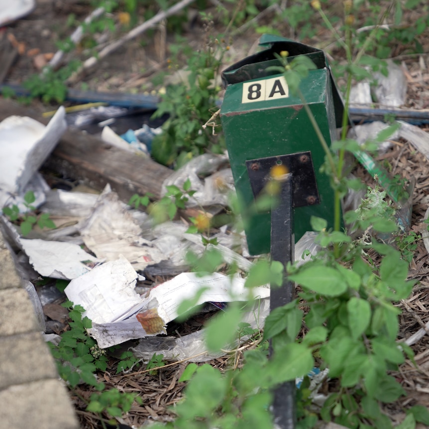 A mailbox lies on the ground among weather damaged envelopes in the grass and dirt.