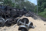 A derailed train lies overturned next to the tracks