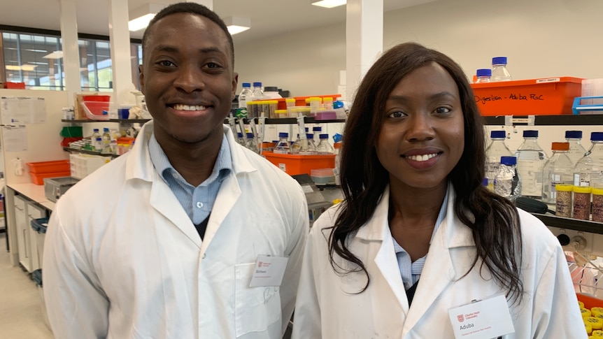 Two PhD students dressed in lab coats smile in science laboratory