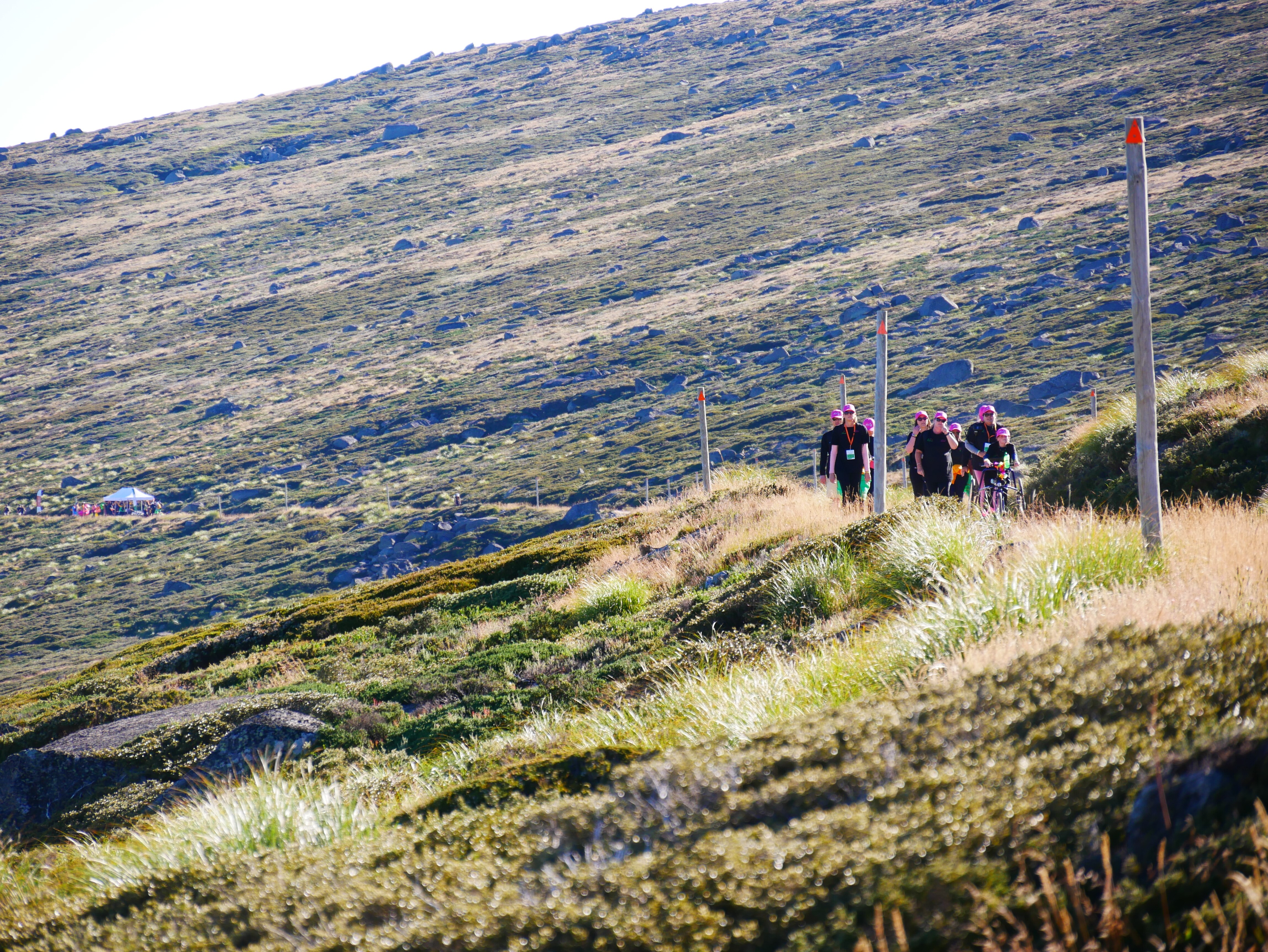 a group of people walk up a hill, with another group far away in the distance