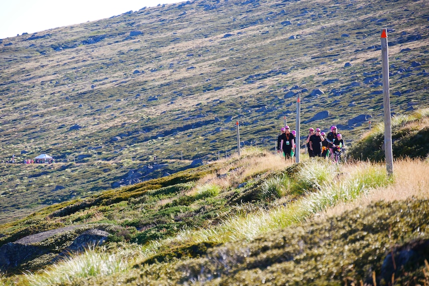 a group of people walk up a hill, with another group far away in the distance