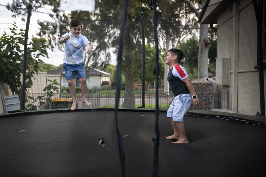Two boys jump on a trampoline.