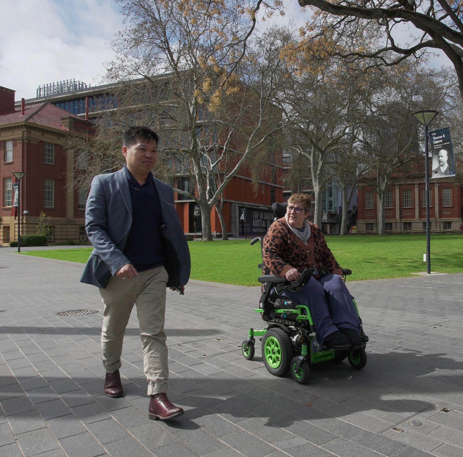Hugo Siu camina junto a una mujer operando su silla de ruedas
