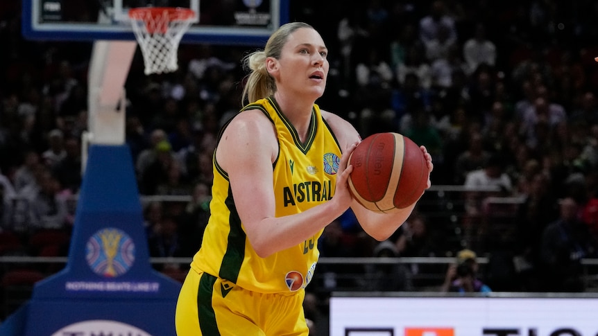 Lauren Jackson wears a green and yellow Australia basketball outfit and is olding a basketball. 