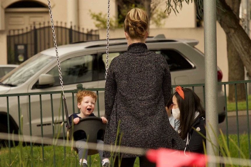 A child on a swing with a woman standing in front of him.