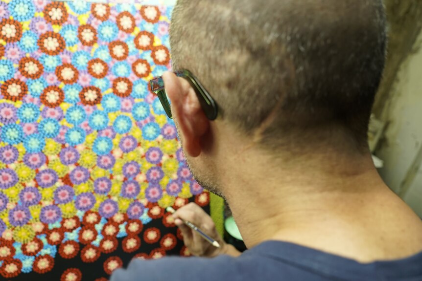The back of Daniels head while he paints an Indigenous artwork