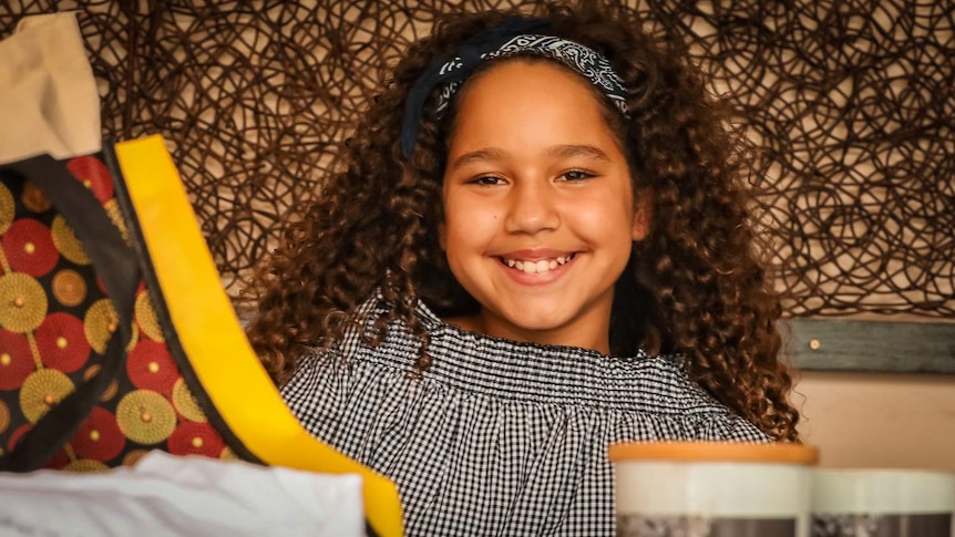 Young indigenous girl Téa Devow is smiling and showcasing traditional products.