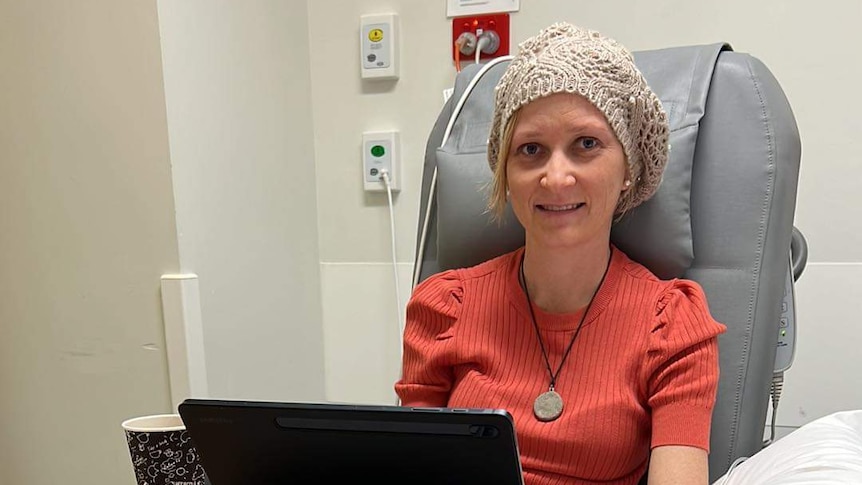 woman sits in cancer chair with beanie and pink shirt
