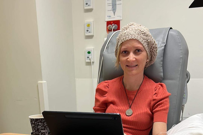 woman sits in cancer chair with beanie and pink shirt