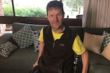 Michael Forbes sits in his lounge room in a wheelchair.