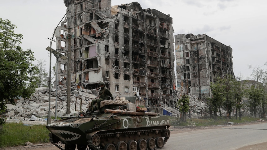 Service members of pro-Russian troops drive an armoured vehicle along a street past a destroyed residential building 