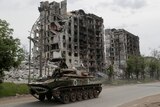 Service members of pro-Russian troops drive an armoured vehicle along a street past a destroyed residential building 