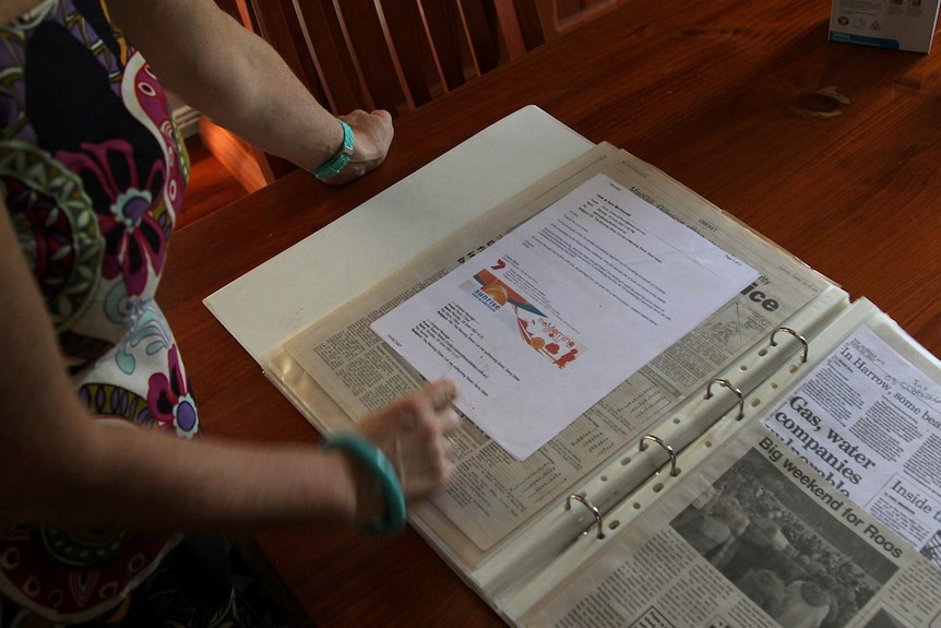 Ange Newton holding open her scrapbook to a page displaying an invite to appear on Sunrise.