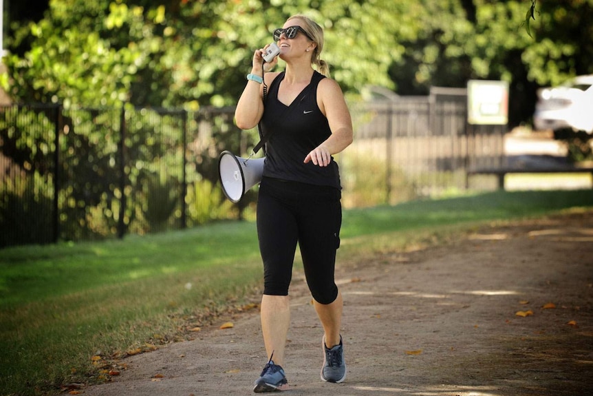 Fitness instructor uses megaphone while demonstrating exercises in a park,