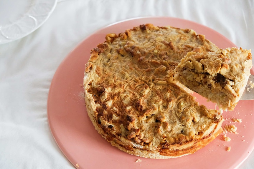 A Bulgarian apple cake on a pink plate with a slice about to be served, an easy and comforting cake recipe.