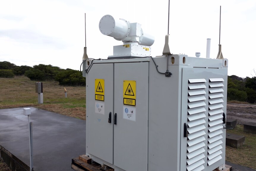 An electrical substation box containing a LiDAR machine, a white box with warning signs and aerials on all four sides.