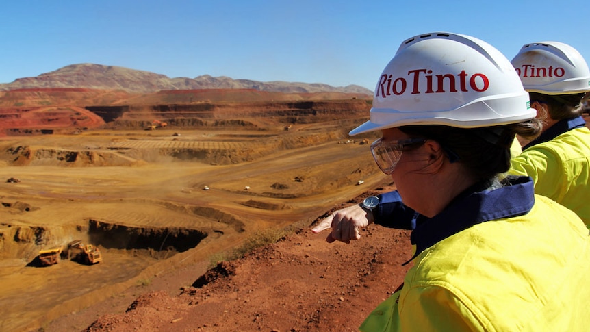 Two workers wearing Rio Tinto hard hats looking out at the West Angelas site in Western Australia.