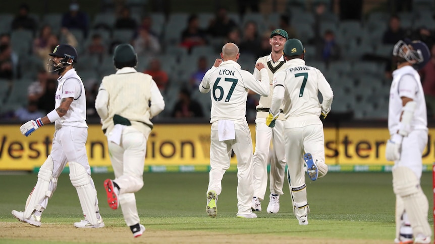 Australian cricketers celebrate as Virat Kohli walks off following a run-out