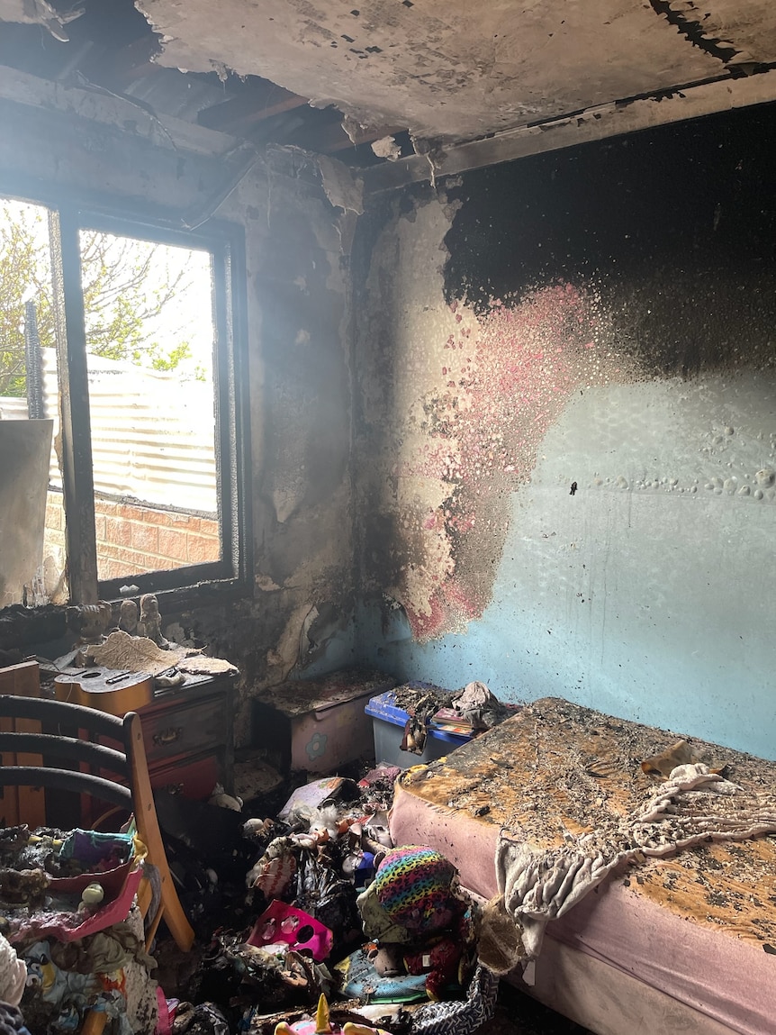 Image of a fire-damaged child's bedroom, the wall and the bed are covered in scorch marks