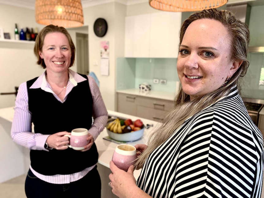 Lindsey Defries and Jessica Mayers stand in their kitchen holding cups of coffee.