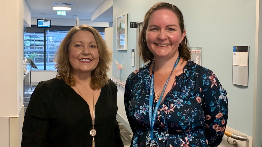 Two women stand smiling in a corridor.