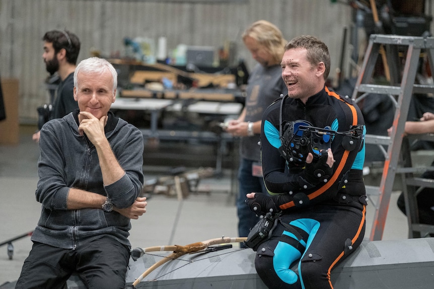 cameron sits beside worthington who is wearing a cgi wet suit looking outfit during filming