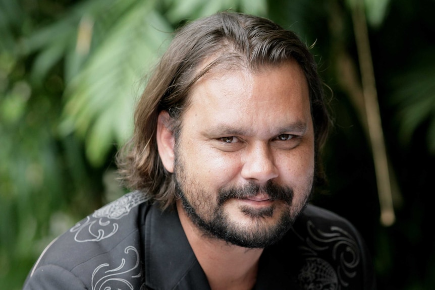 Thornton, a man in his mid-forties with shoulder length brown hair and a short beard smiles into the camera.