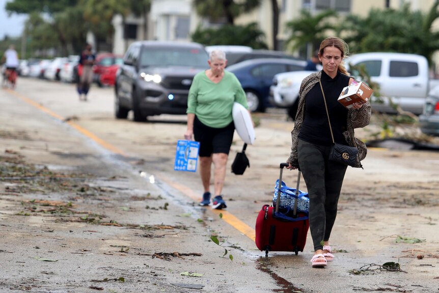 A woman pulls a suitcase down a street that is covered in debris. 