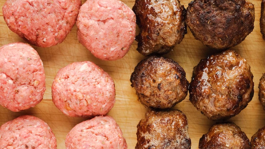 A group of raw and cooked meatballs sitting on a cutting board.