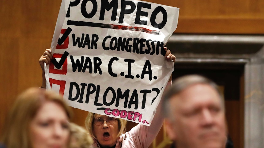 A woman holds up a protest sign inside Mike Pompeo's confirmation hearing.