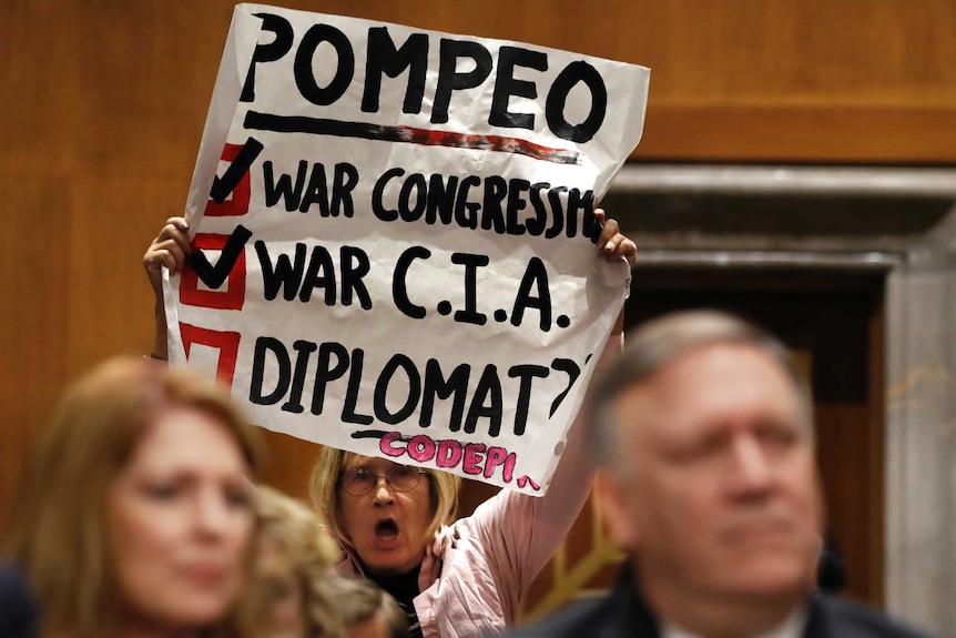 A woman holds up a protest sign inside Mike Pompeo's confirmation hearing.