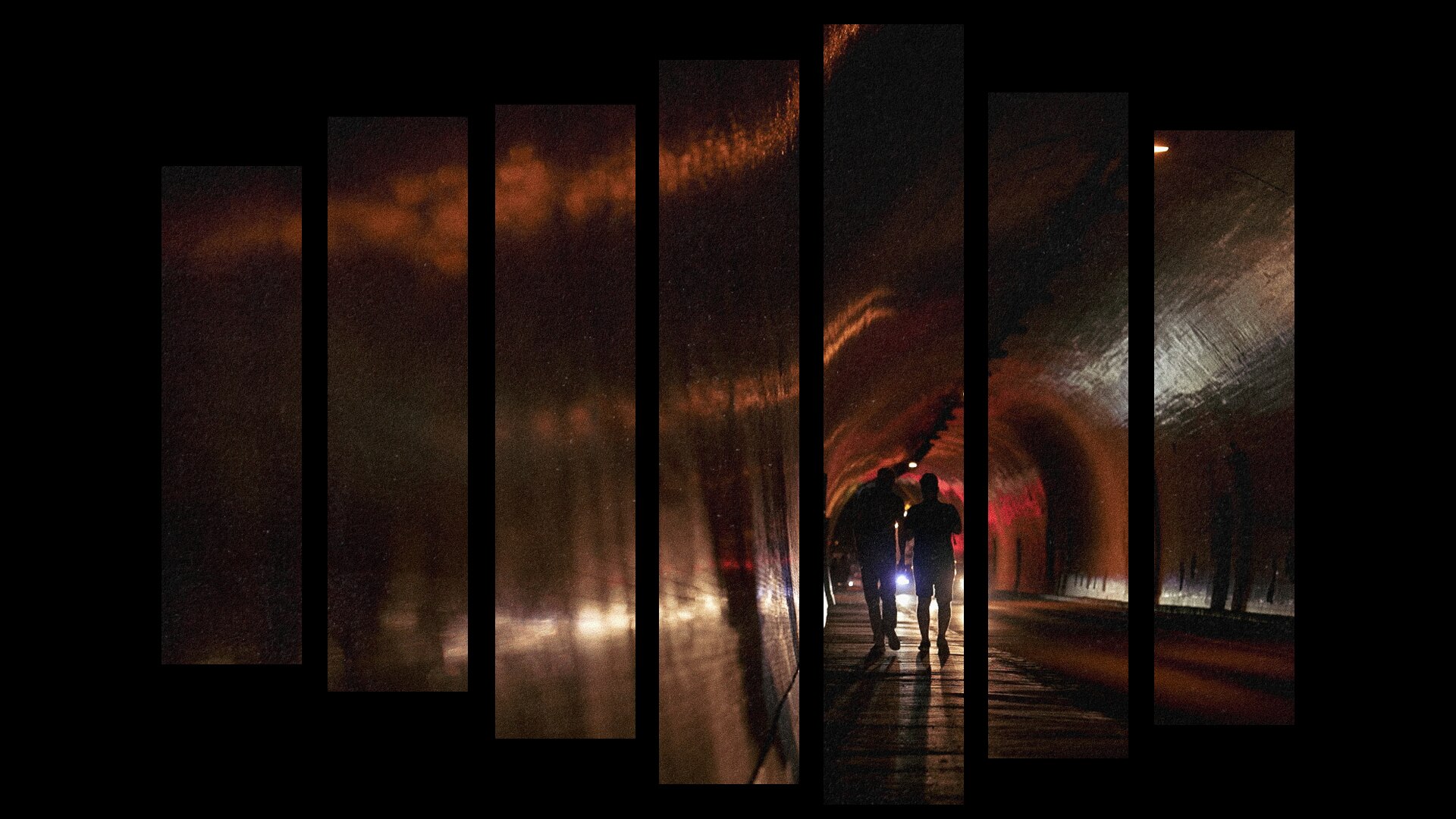 Two people are silhouetted by car headlights at night as they walk down a footpath in a large tunnel.