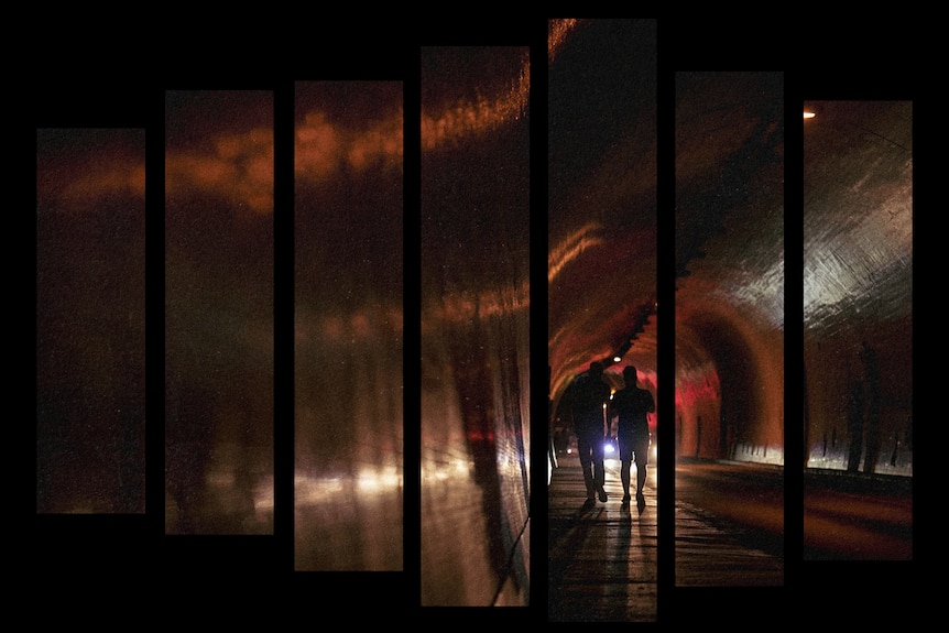 Two people are silhouetted by car headlights at night as they walk down a footpath in a large tunnel.