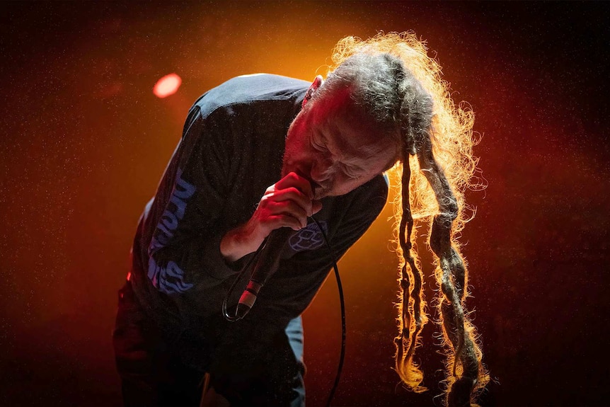 Close up photo of dreadlocked Frenzal Rhomb singer Jay Whalley leaning over and screaming into a microphone